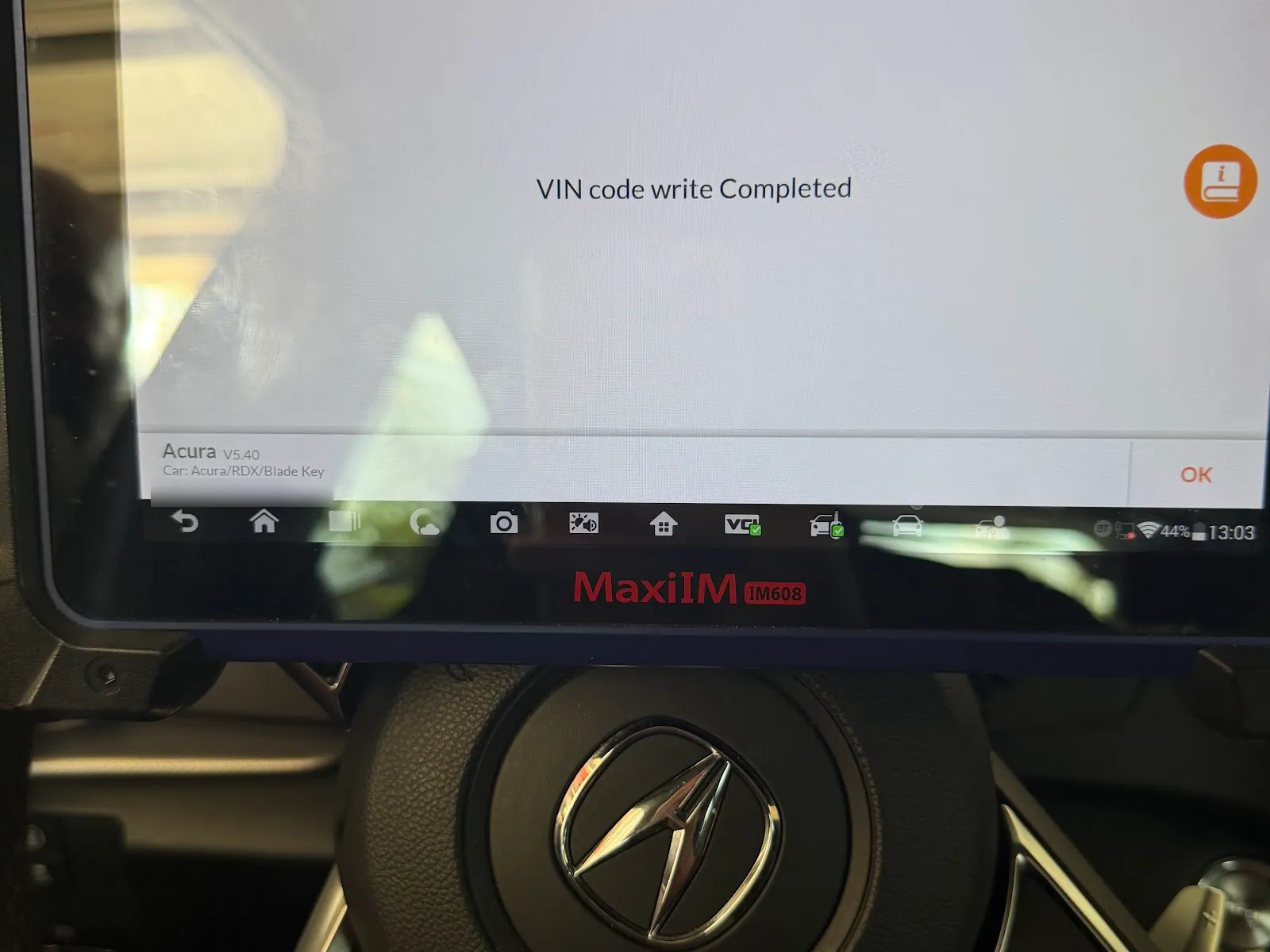A key programming tablet held in front of an Acura steering wheel during a car key job